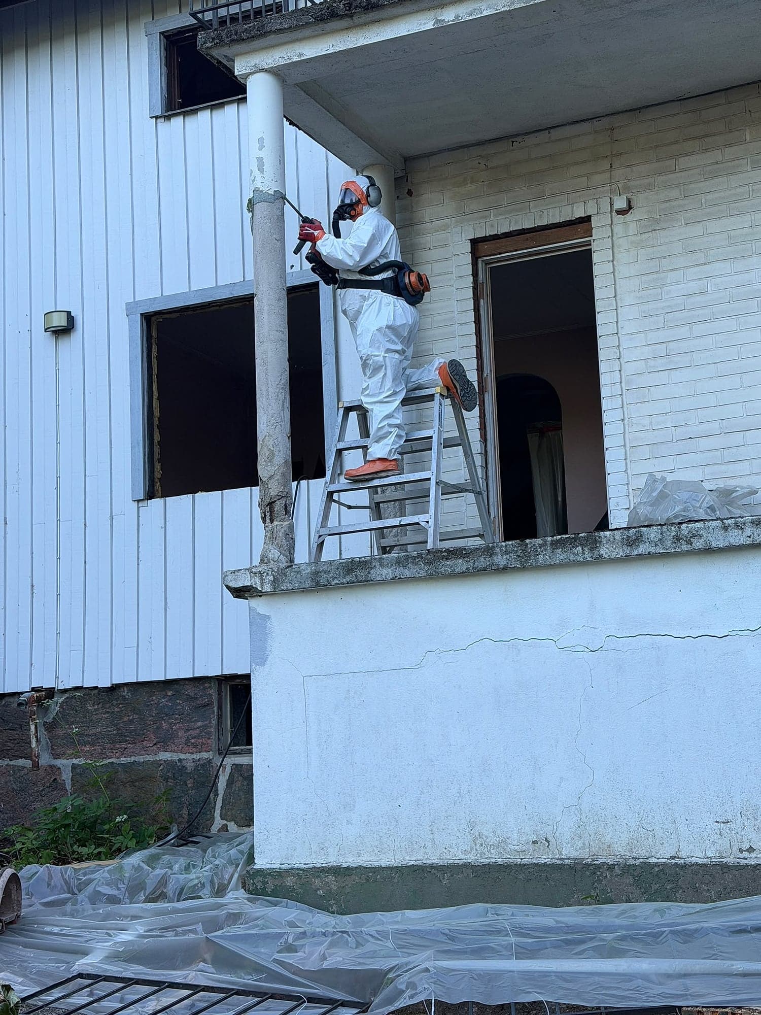 Person i skyddsdräkt och andningsskydd arbetar vid en husfasad.